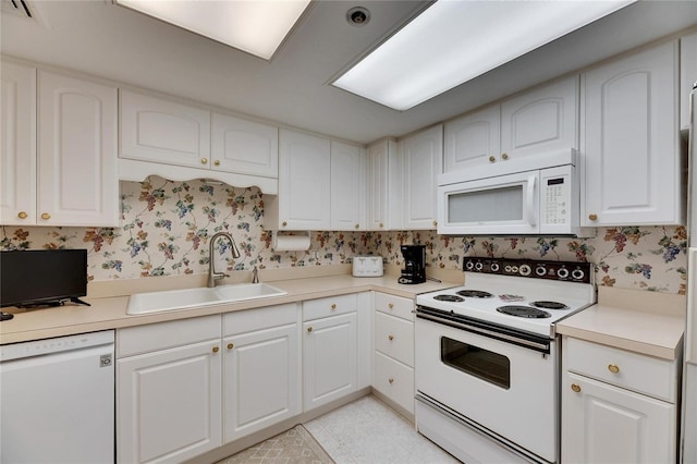 kitchen featuring white appliances, a sink, white cabinetry, light countertops, and wallpapered walls