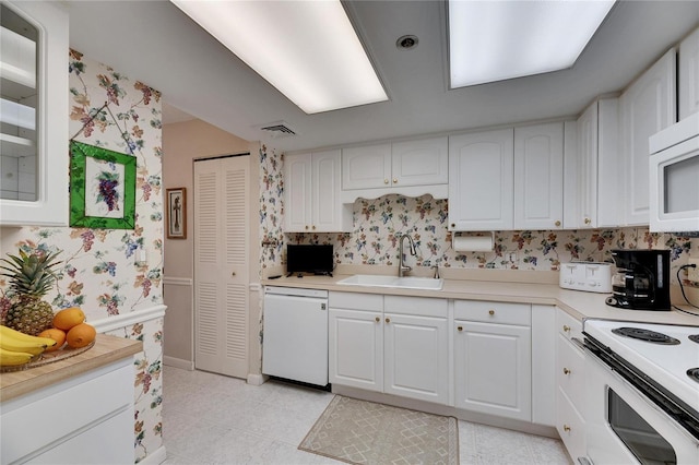 kitchen with white appliances, a sink, white cabinetry, and wallpapered walls