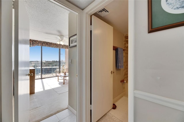 interior space with visible vents, a ceiling fan, a textured ceiling, baseboards, and tile patterned floors