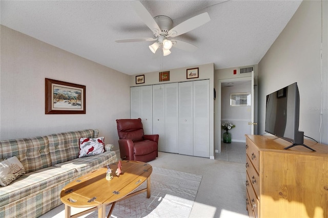 living room with light colored carpet, visible vents, ceiling fan, and a textured ceiling