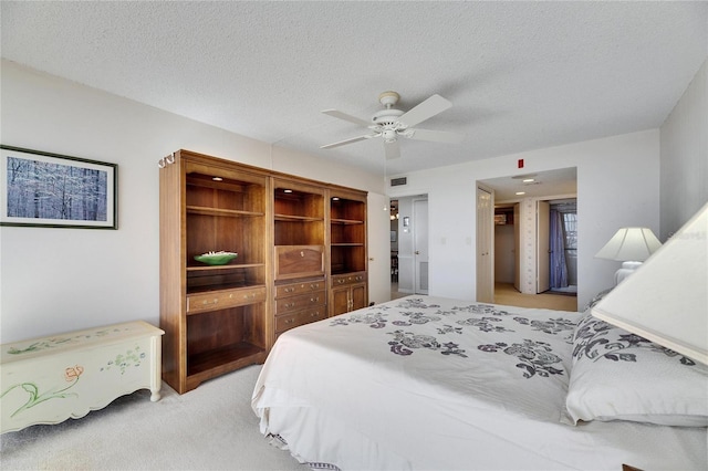 bedroom with light carpet, a ceiling fan, visible vents, and a textured ceiling