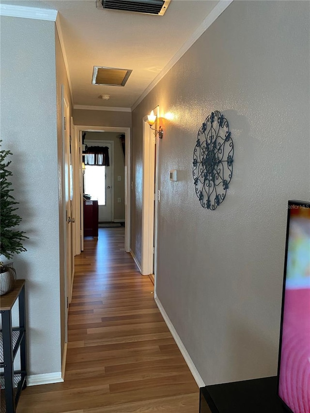 hallway featuring a textured wall, wood finished floors, visible vents, baseboards, and ornamental molding