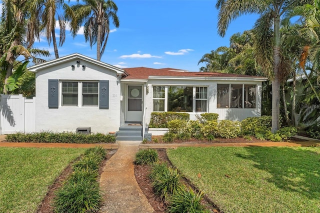 bungalow with a front yard, fence, a sunroom, and stucco siding