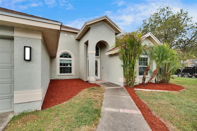 view of front of home with a garage, a front yard, and stucco siding