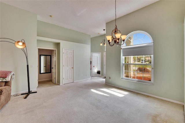 carpeted empty room with plenty of natural light, high vaulted ceiling, a chandelier, and baseboards