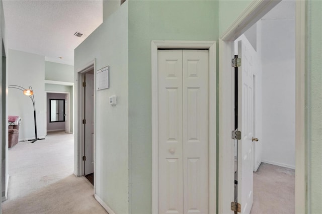 hall featuring light carpet, visible vents, baseboards, and a textured ceiling