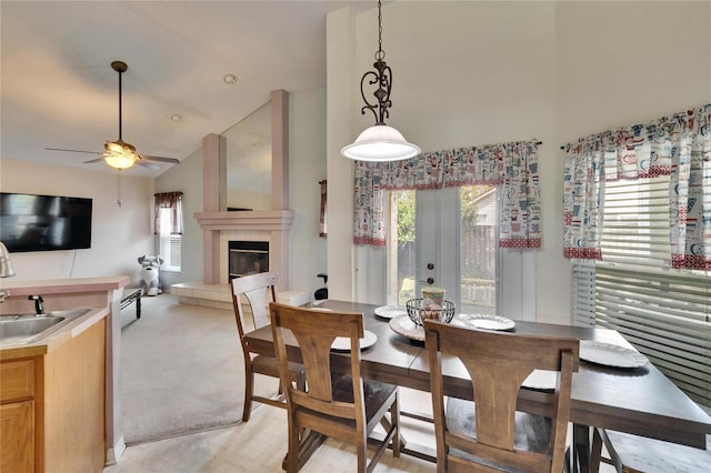 dining area featuring ceiling fan, high vaulted ceiling, light carpet, french doors, and a tiled fireplace