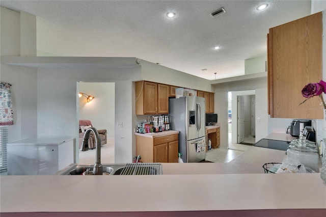 kitchen with visible vents, brown cabinets, light countertops, stainless steel refrigerator with ice dispenser, and a sink