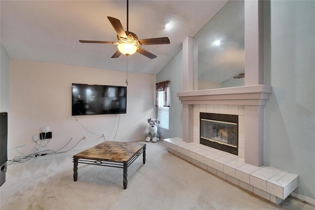 living area featuring vaulted ceiling, carpet floors, a tiled fireplace, and a ceiling fan