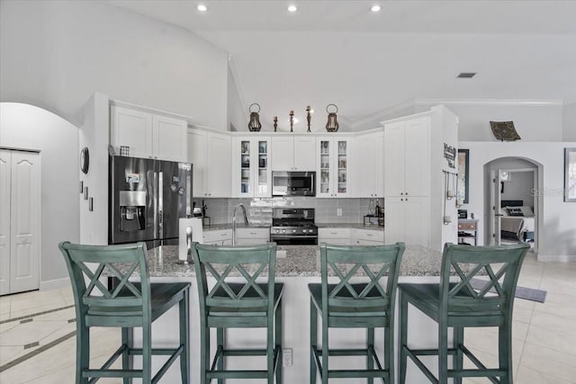 kitchen with decorative backsplash, white cabinets, arched walkways, and appliances with stainless steel finishes