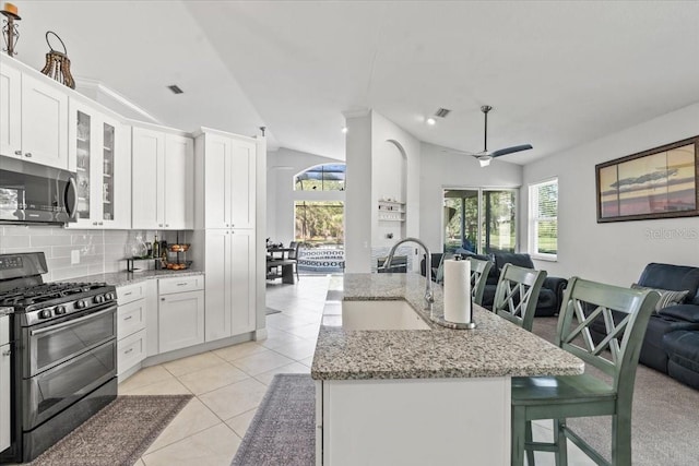 kitchen with a sink, backsplash, open floor plan, appliances with stainless steel finishes, and light tile patterned floors