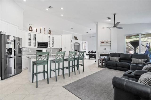 living area featuring light tile patterned floors, a ceiling fan, visible vents, and high vaulted ceiling