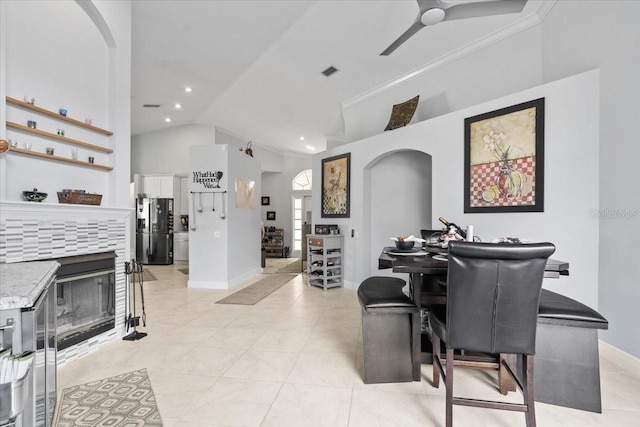 dining area featuring visible vents, crown molding, ceiling fan, a tiled fireplace, and arched walkways