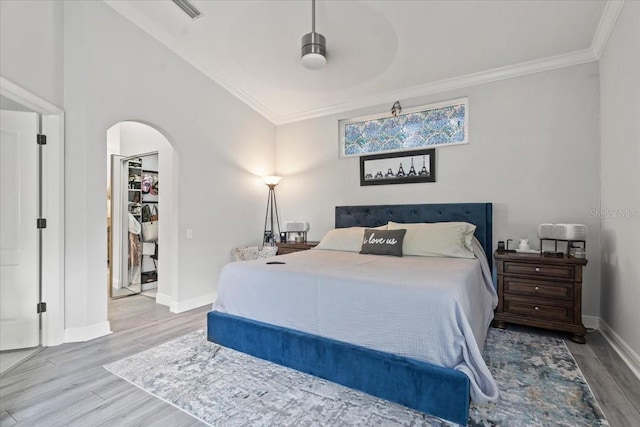 bedroom featuring baseboards, wood finished floors, arched walkways, and ornamental molding