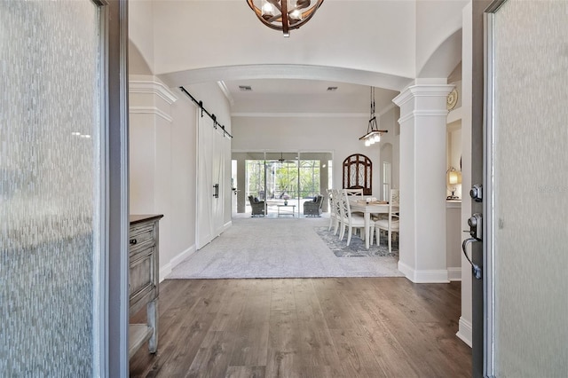 foyer with arched walkways, crown molding, decorative columns, a barn door, and wood finished floors