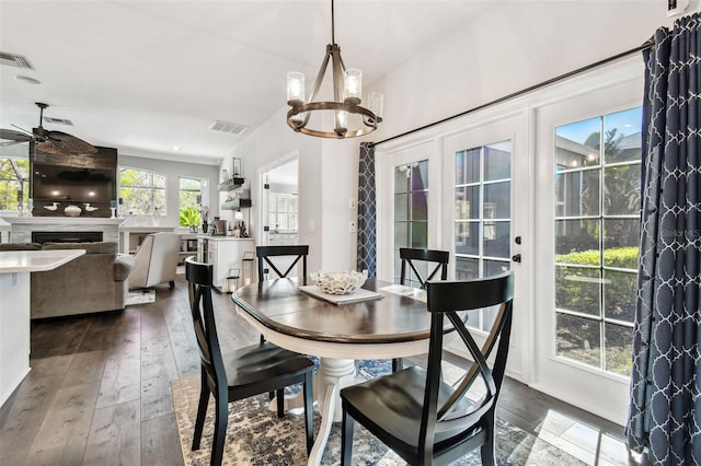 dining space featuring ceiling fan with notable chandelier, dark wood-type flooring, a fireplace, and visible vents