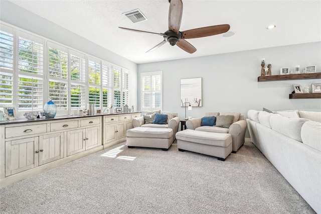 living room featuring a textured ceiling, recessed lighting, light colored carpet, a ceiling fan, and visible vents