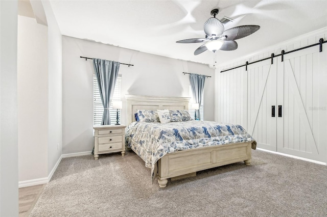 bedroom featuring a barn door, visible vents, baseboards, a ceiling fan, and carpet floors