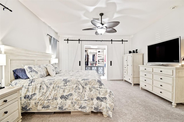 bedroom with ceiling fan, a barn door, and light colored carpet