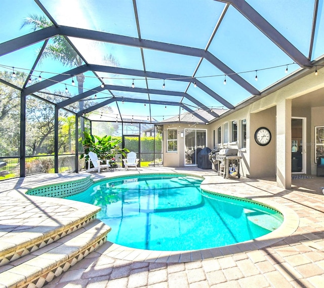 outdoor pool with a patio area, glass enclosure, and grilling area