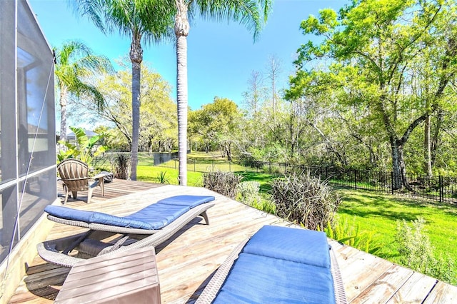 wooden terrace featuring a lanai, fence, and a lawn