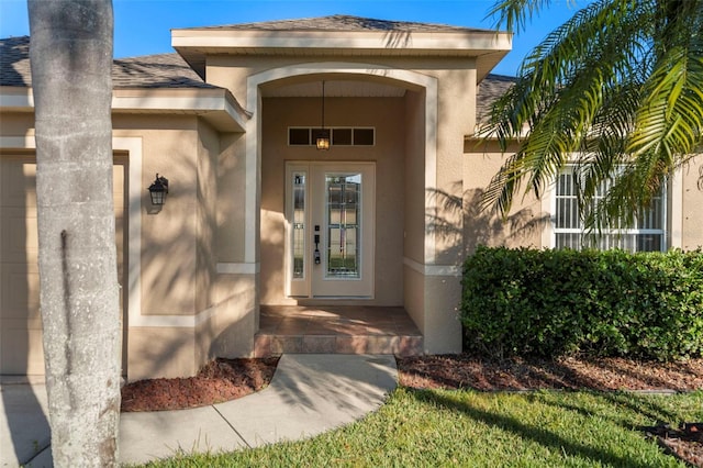 view of exterior entry featuring roof with shingles, an attached garage, and stucco siding