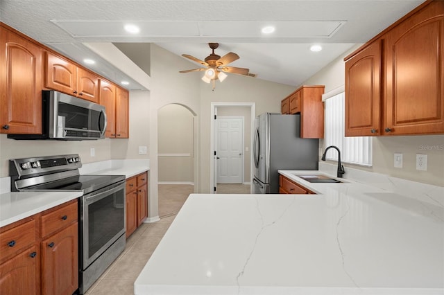 kitchen featuring lofted ceiling, light stone counters, stainless steel appliances, and a sink