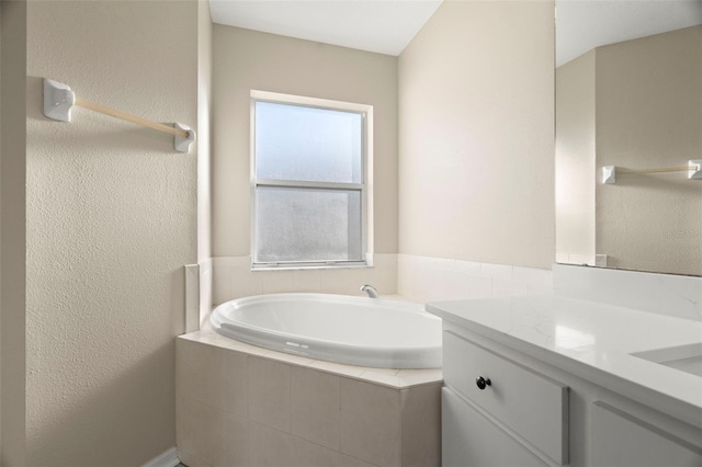 full bath with a textured wall, a garden tub, and vanity