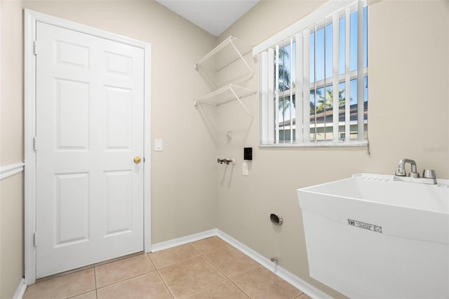 clothes washing area featuring light tile patterned floors, laundry area, a sink, and baseboards