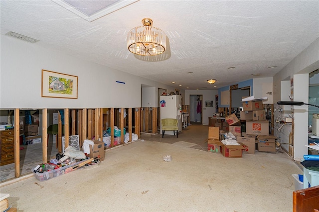 basement with visible vents, white fridge with ice dispenser, a notable chandelier, and a textured ceiling