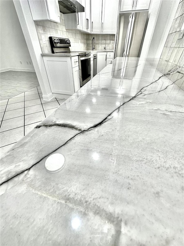 kitchen featuring light stone counters, a sink, stainless steel appliances, wall chimney exhaust hood, and backsplash