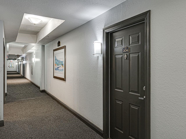 corridor with a textured wall, baseboards, and dark colored carpet