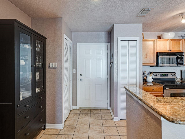 kitchen featuring light tile patterned flooring, light stone counters, appliances with stainless steel finishes, a textured ceiling, and visible vents