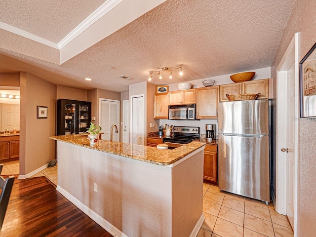 kitchen featuring crown molding, light stone countertops, a textured ceiling, a center island with sink, and stainless steel appliances