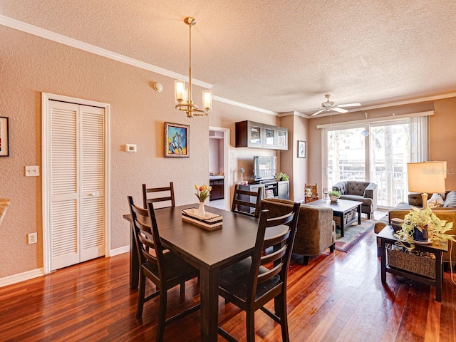 dining room featuring dark wood-style flooring, ornamental molding, a textured wall, and ceiling fan with notable chandelier