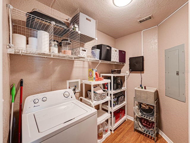 clothes washing area featuring electric panel, a textured wall, washer / dryer, laundry area, and wood finished floors