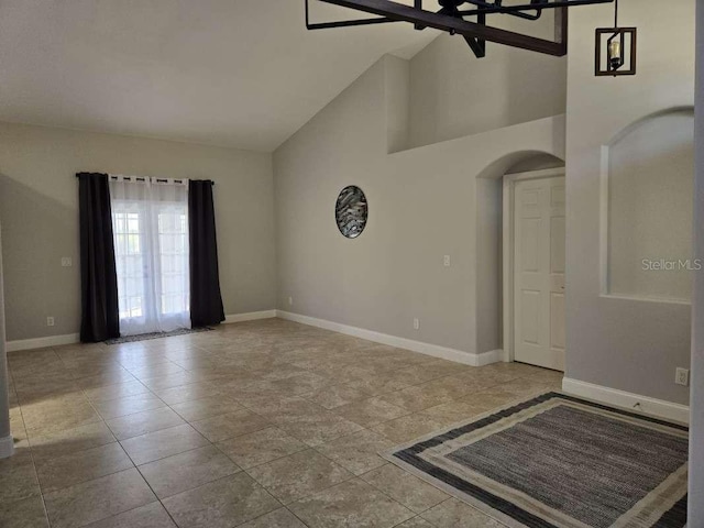 spare room featuring arched walkways, high vaulted ceiling, tile patterned flooring, and baseboards