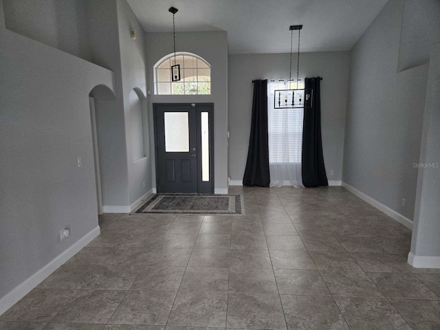 foyer entrance with arched walkways, tile patterned floors, and baseboards