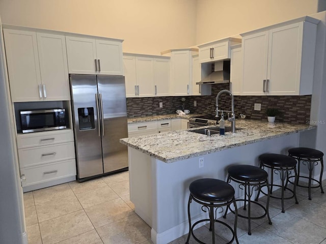 kitchen with decorative backsplash, appliances with stainless steel finishes, a peninsula, wall chimney range hood, and a sink