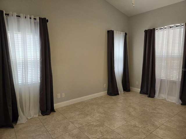 unfurnished room with lofted ceiling, light tile patterned flooring, and baseboards