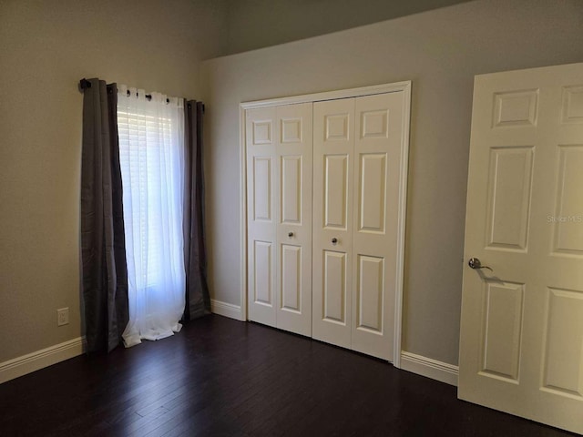 unfurnished bedroom featuring dark wood-type flooring, a closet, and baseboards