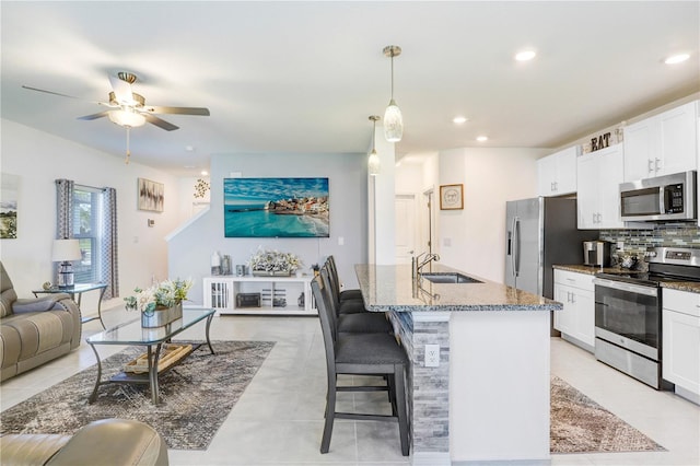 kitchen with stone counters, backsplash, appliances with stainless steel finishes, open floor plan, and a sink