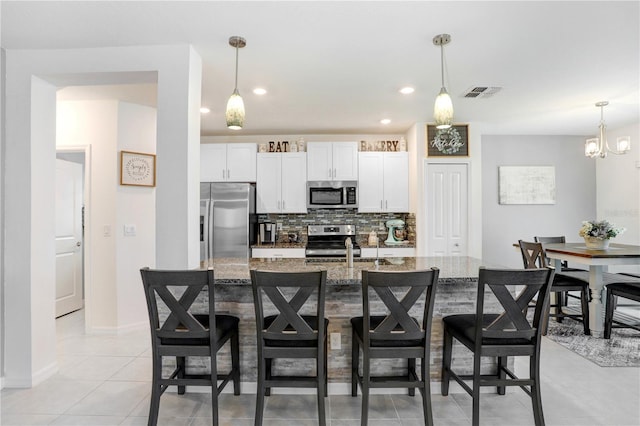 kitchen with light stone counters, visible vents, appliances with stainless steel finishes, decorative backsplash, and a kitchen bar