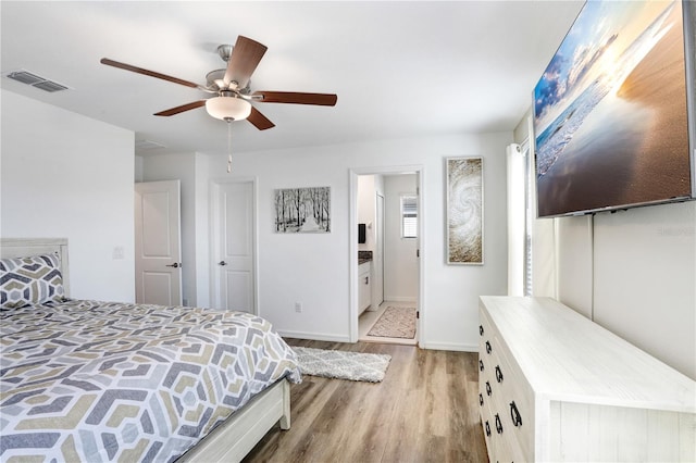 bedroom featuring light wood finished floors, baseboards, visible vents, a ceiling fan, and ensuite bathroom