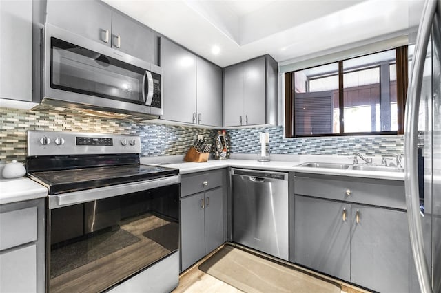 kitchen featuring gray cabinetry, a sink, light countertops, appliances with stainless steel finishes, and backsplash