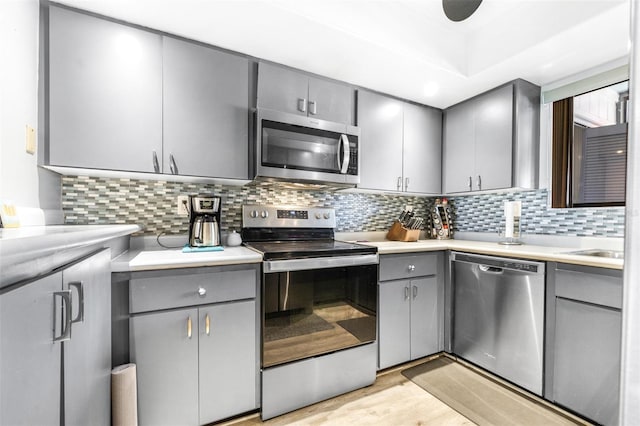 kitchen featuring light countertops, appliances with stainless steel finishes, light wood-type flooring, gray cabinets, and decorative backsplash