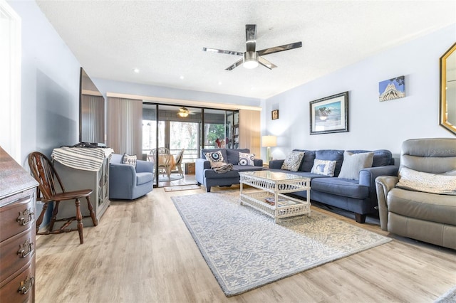 living room featuring light wood-type flooring, ceiling fan, and a textured ceiling