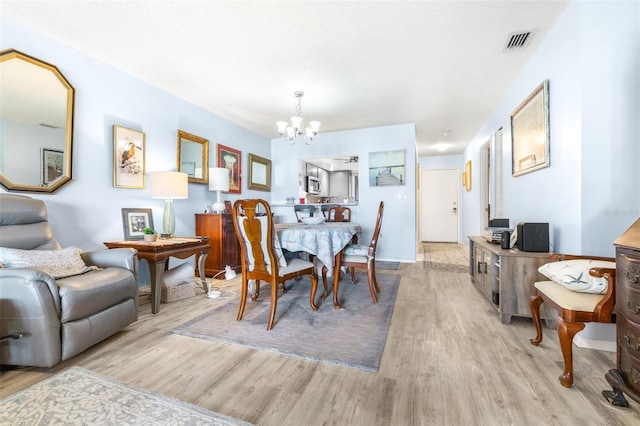 dining space with wood finished floors, visible vents, and an inviting chandelier