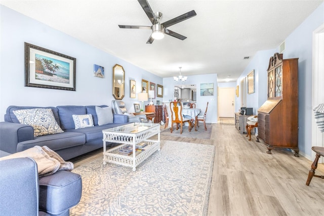 living room featuring ceiling fan with notable chandelier, visible vents, a textured ceiling, and light wood-style flooring