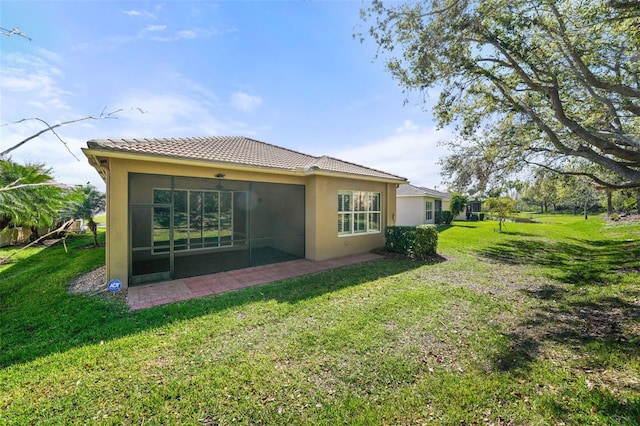 rear view of house with stucco siding, a tiled roof, a yard, and a sunroom